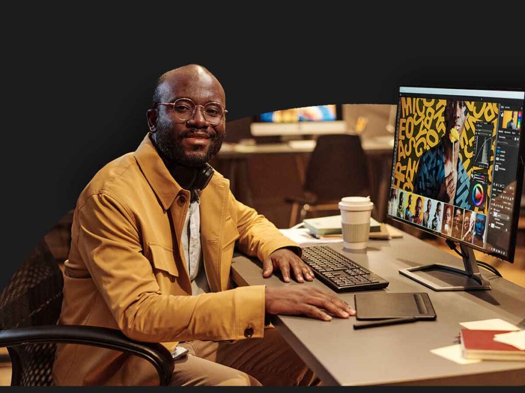 A Man Sitting At A Desk With A Computer