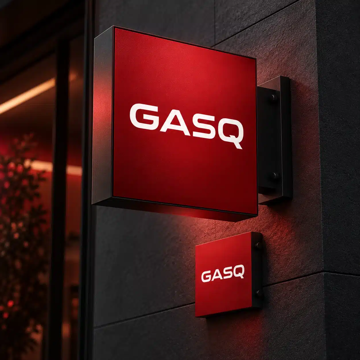 GASQ dimensional brand signage application concept. Dramatic close view of an elegant projecting square wayfinding sign, matte rich red face and exact white GASQ wordmark taken from reference social creative, mounted on dark charcoal architectural wall. Secondary smaller red wayfinding panel beneath uses only GASQ again. Strong dimensional materials, soft red light bounce, sophisticated high-end identity presentation. Do not copy IREB logo or social campaign text. No invented location, no claims of an actual installed office. No screens.. Brand application concept.